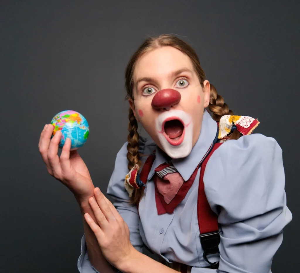 Pamela Pilawa in Clown Costume posing with a globe showcasing family friendly theatre shows in Sydney