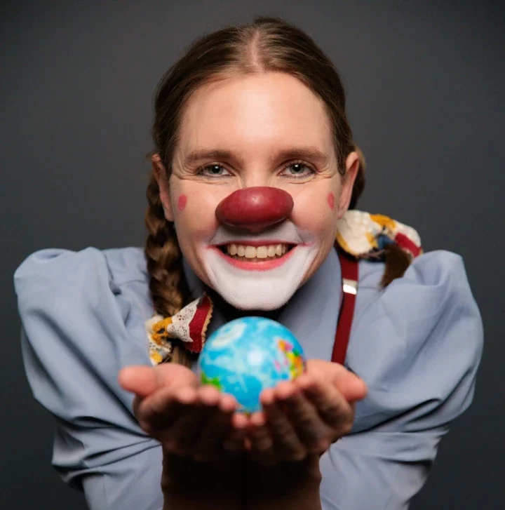 Pamela Pilawa in Clown Costume posing with a globe showcasing her family friendly theatre shows in Sydney